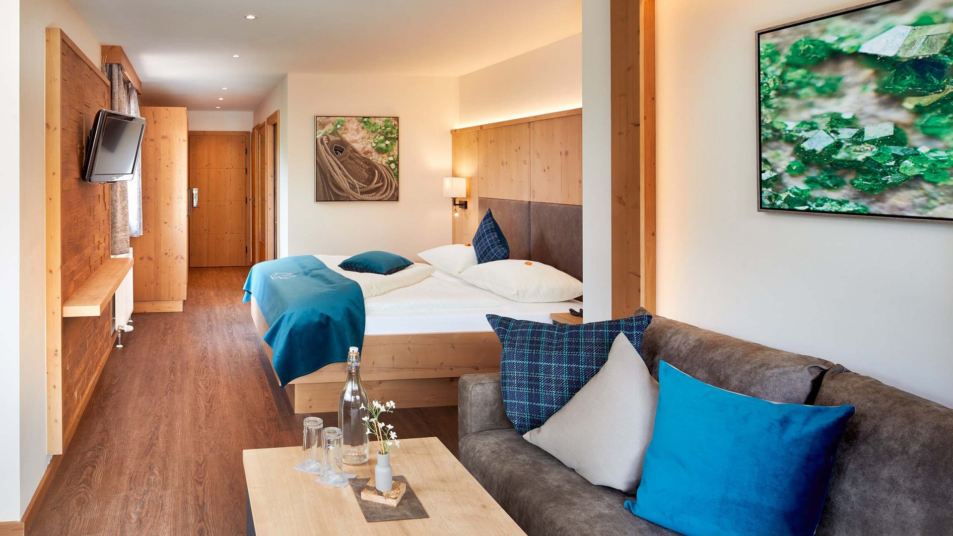 Smaragdhotel Tauernblick – Ihr 4-Sterne-Hotel am Wildkogel Modernes Hotelzimmer mit Doppelbett, Sofa und TV mit Naturdekorationen