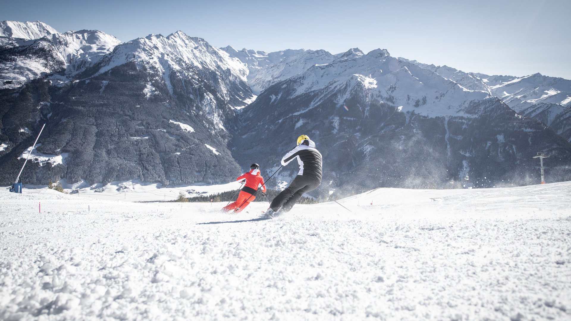 Smaragdhotel Tauernblick – Ihr 4-Sterne-Hotel am Wildkogel Zwei Skifahrer fahren bei Sonnenschein auf verschneiter Piste mit Bergkulisse
