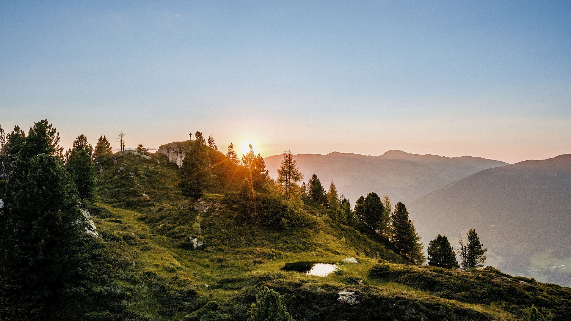Smaragdhotel Tauernblick – Ihr 4-Sterne-Hotel am Wildkogel Sonnenuntergang in den Bergen mit einer hügeligen Landschaft und Bäumen