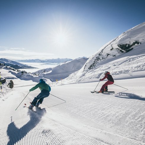 Smaragdhotel Tauernblick – Ihr 4-Sterne-Hotel am Wildkogel Zwei Skifahrer fahren bei sonnigem Wetter auf einer präparierten Skipiste