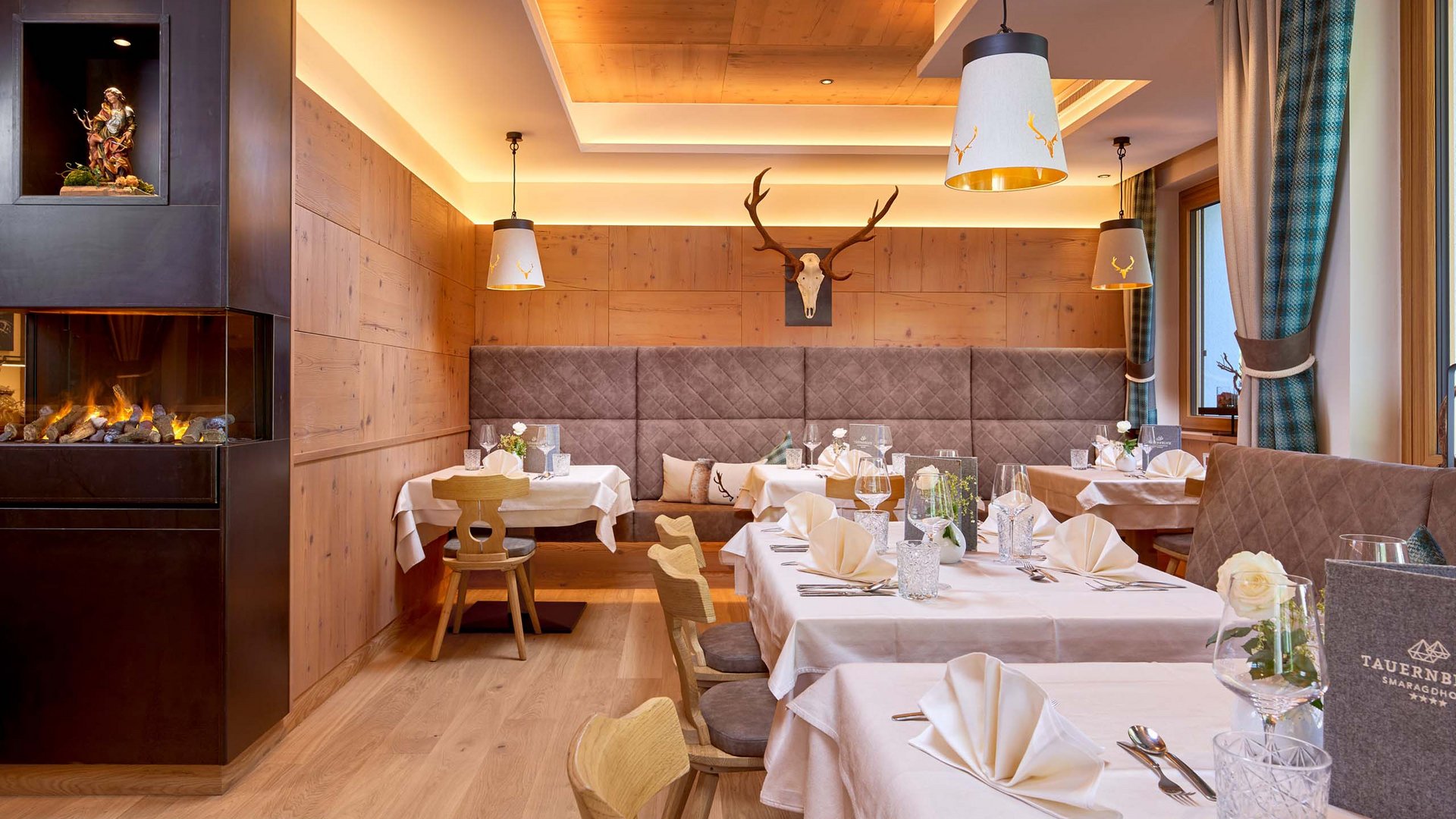 Smaragdhotel Tauernblick – Ihr 4-Sterne-Hotel am Wildkogel Gemütliches Restaurant mit Holzwänden, Kamin und gedeckten Tischen